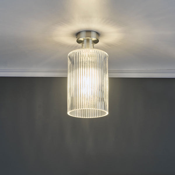 A modern ceiling light with a brushed nickel base and a fluted glass shade, casting light upwards.