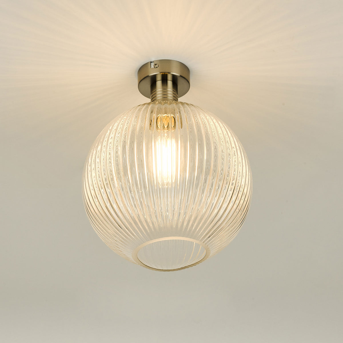 Round, ribbed glass ceiling light with a brushed nickel base, casting a warm glow on the white ceiling.