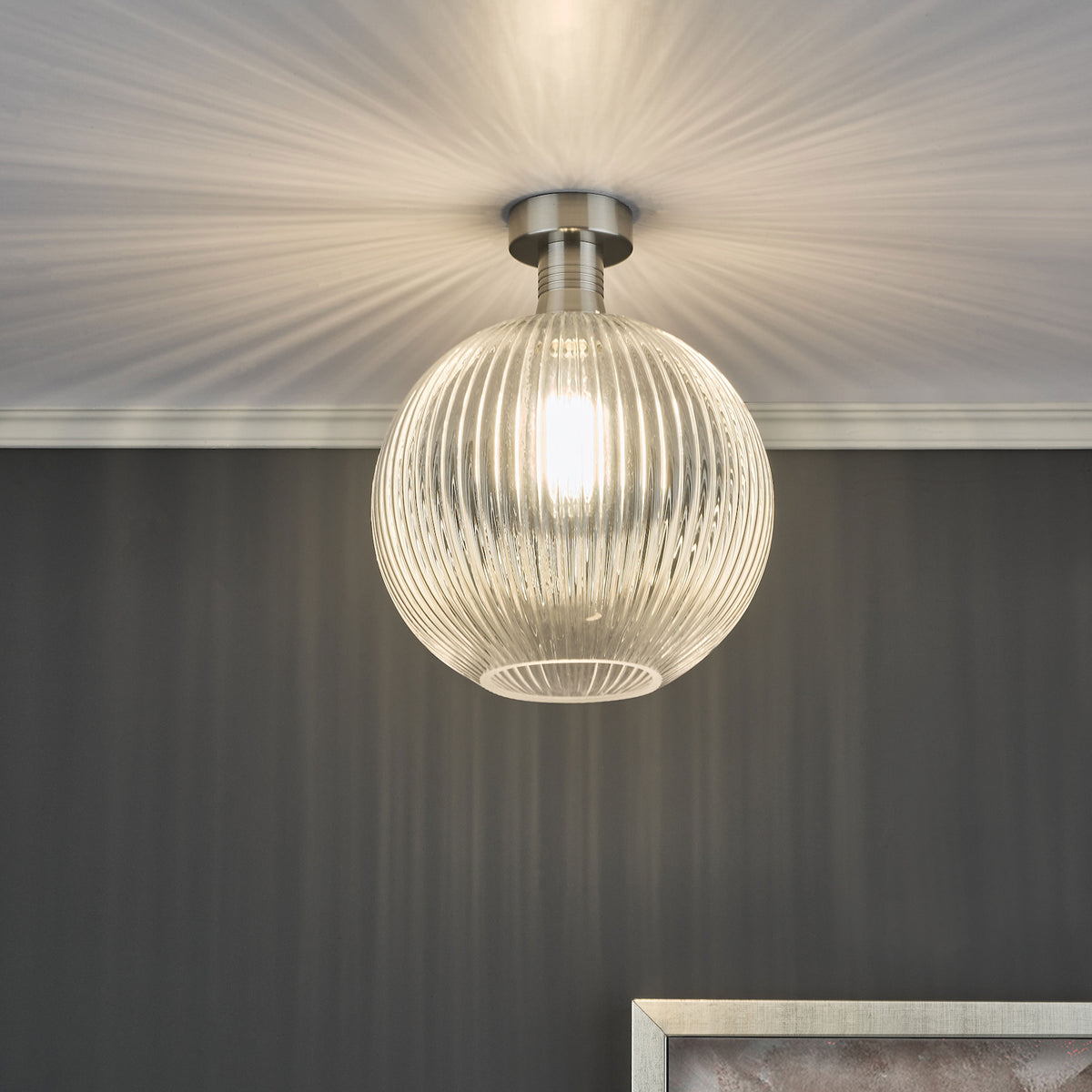 A clear, ribbed glass ceiling light illuminates a dark gray wall, casting radial light patterns.
