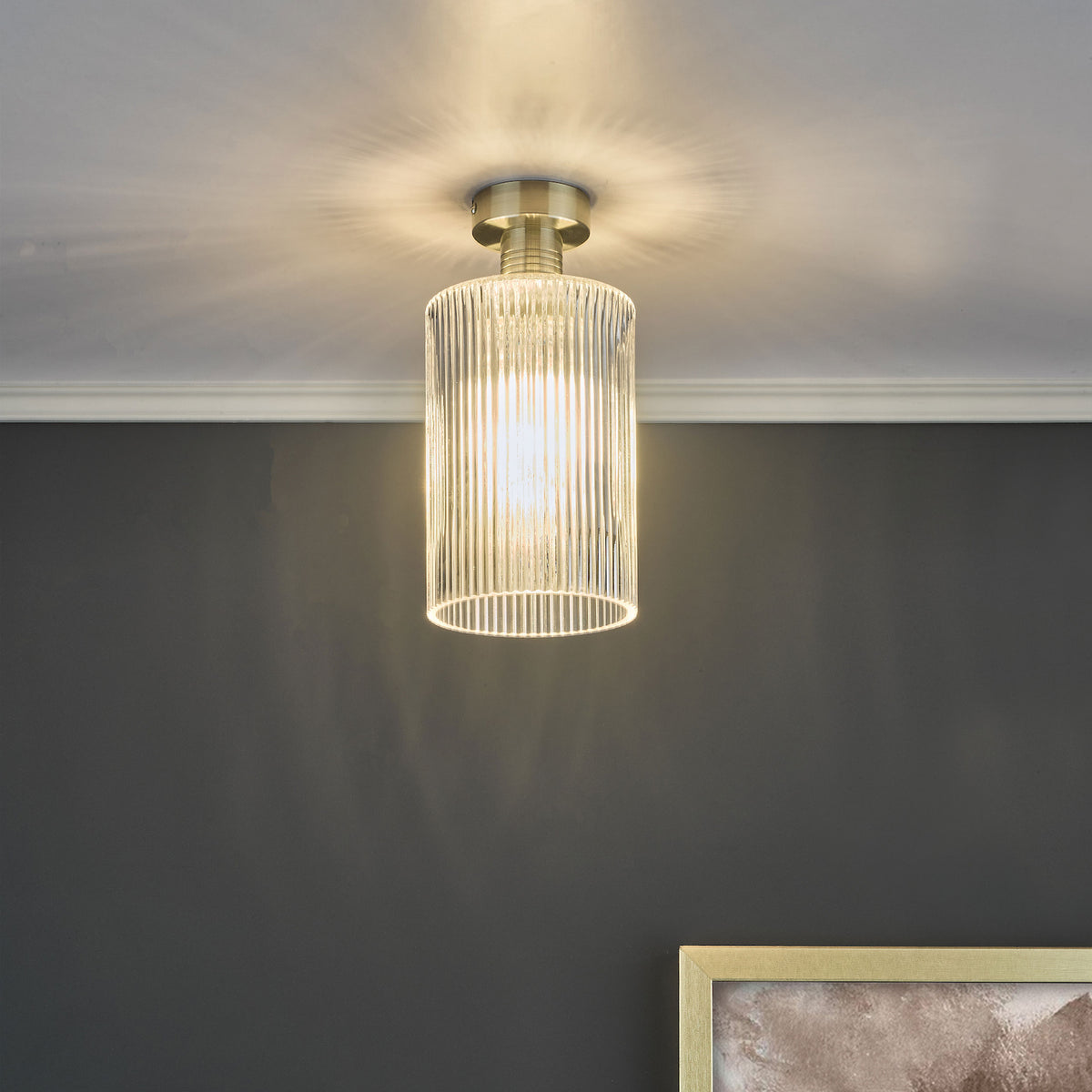 A brass ceiling light with a ribbed glass shade illuminates a dark gray wall and white crown molding.