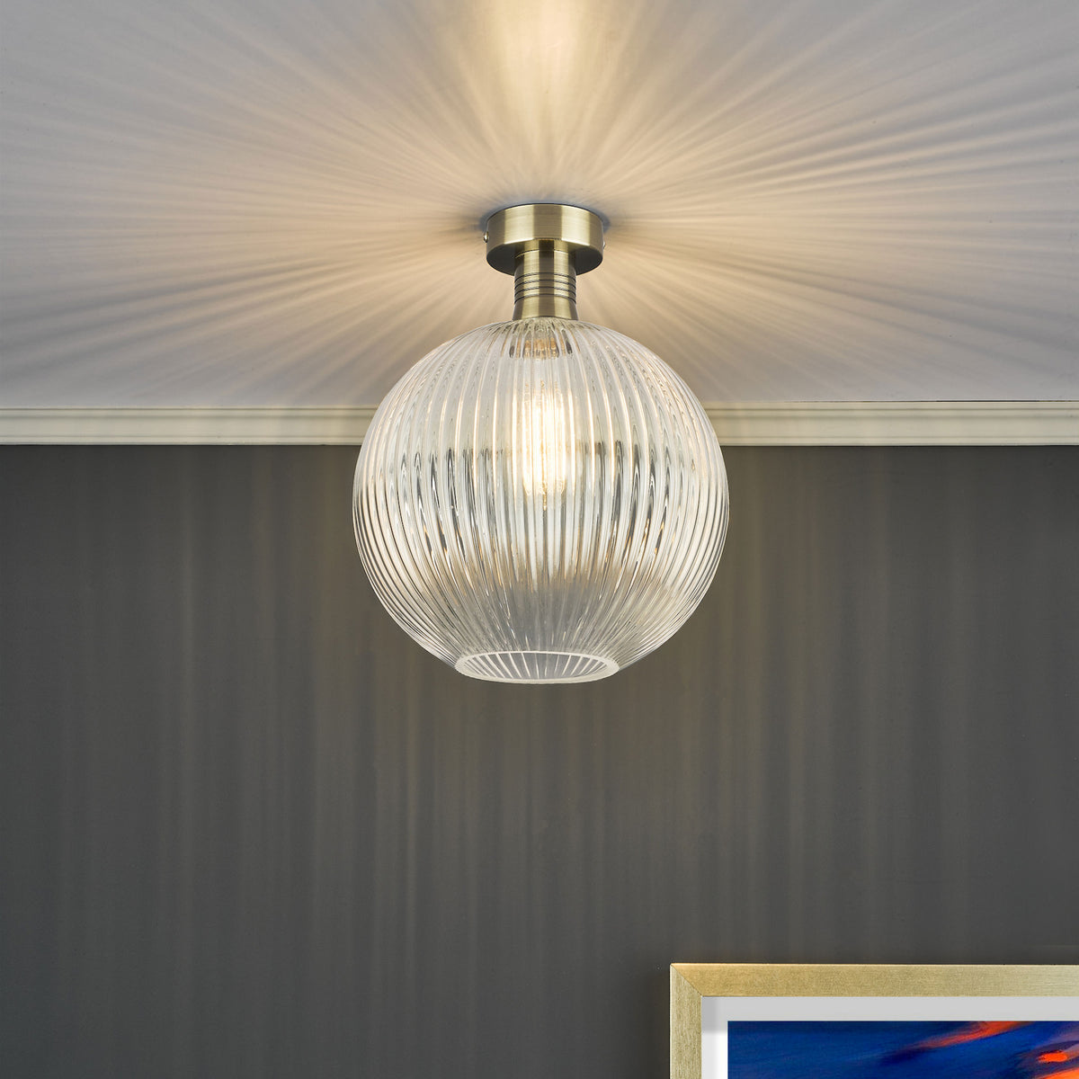 A close-up of a ceiling light with a ribbed glass shade and a brass base, casting radial light patterns.