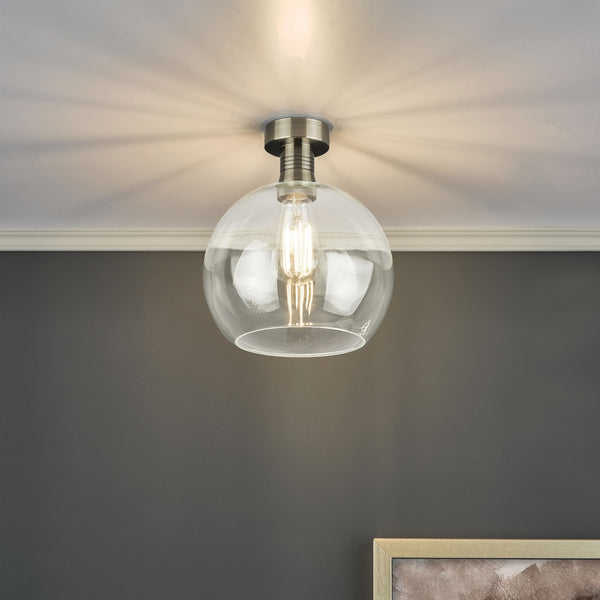 A clear glass globe ceiling light with a brushed nickel base and an exposed filament bulb.
