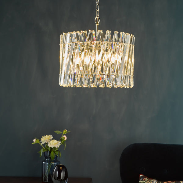 Rectangular crystal chandelier with a gold chain, dark blue wall, and flowers in a vase