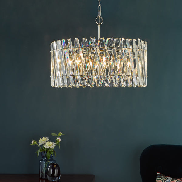 Rectangular crystal chandelier with faceted prisms and a gold chain, hanging against a dark teal wall
