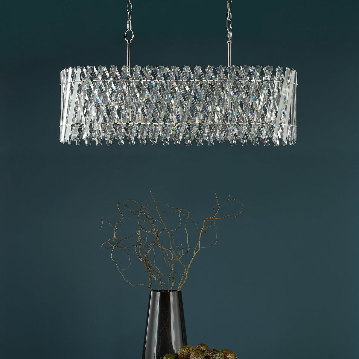 Rectangular crystal chandelier with silver chains above a black vase with branches