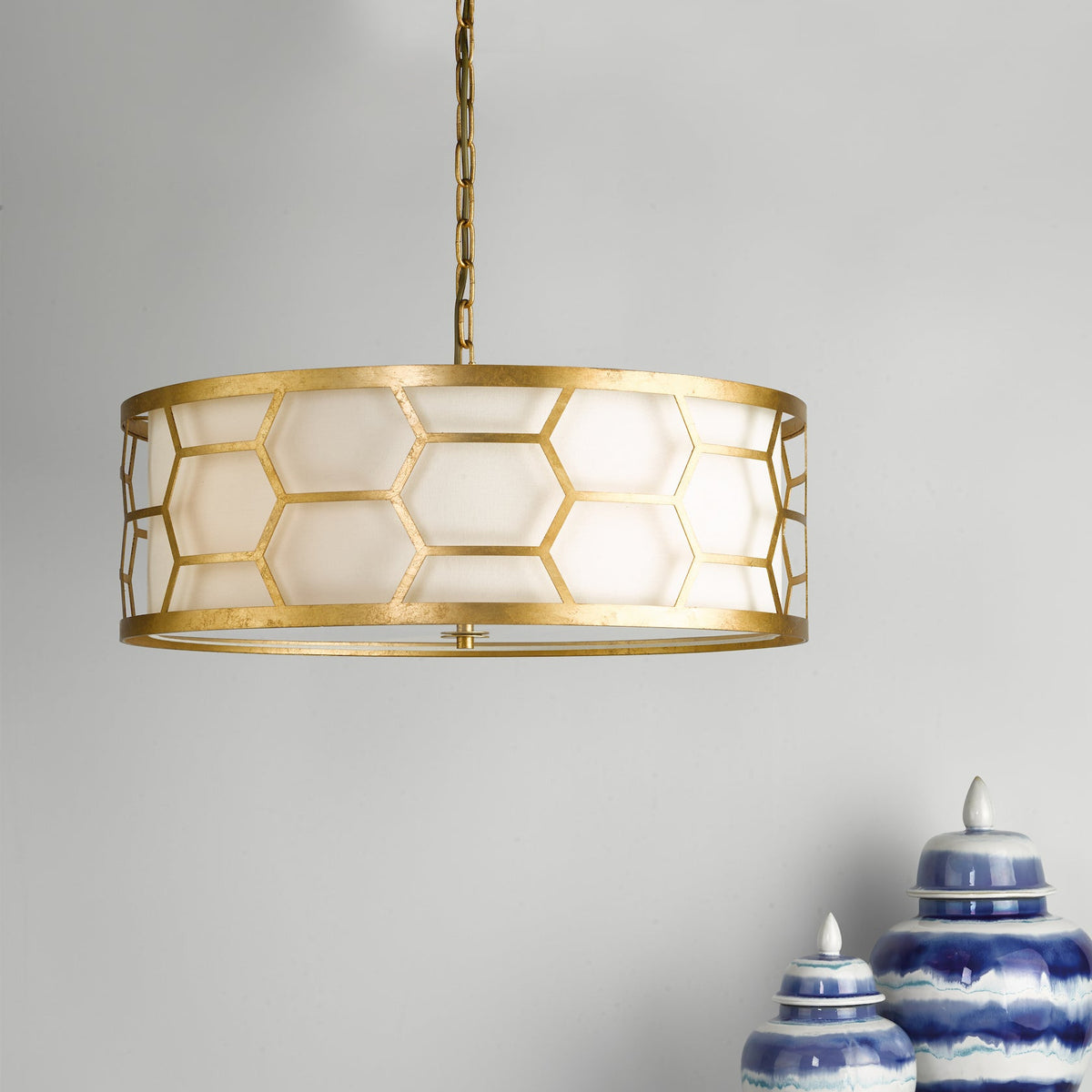 Gold chandelier with a white drum shade and a geometric honeycomb pattern