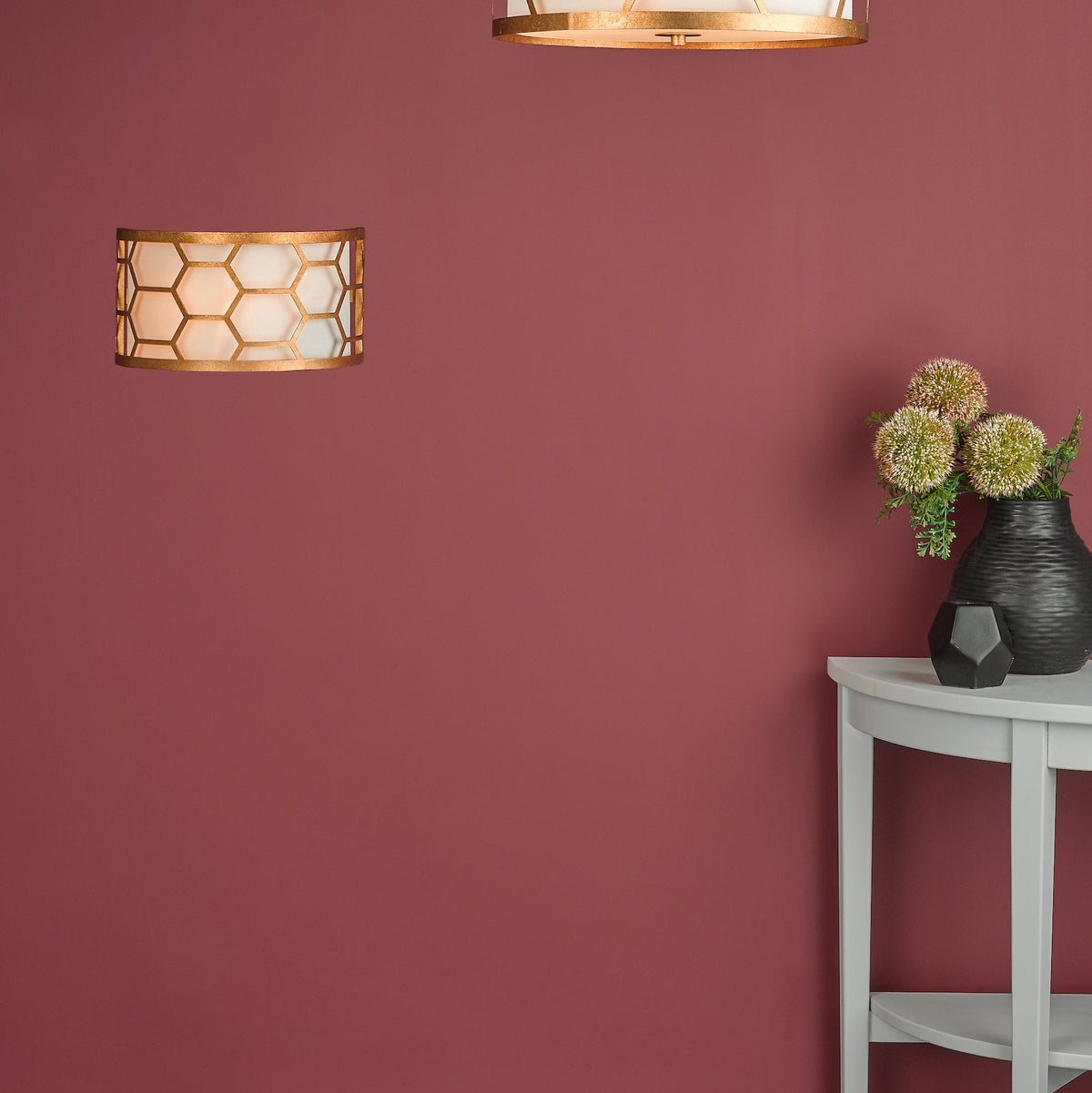 Gold honeycomb wall sconce and ceiling light on a red wall, with a grey half-moon table