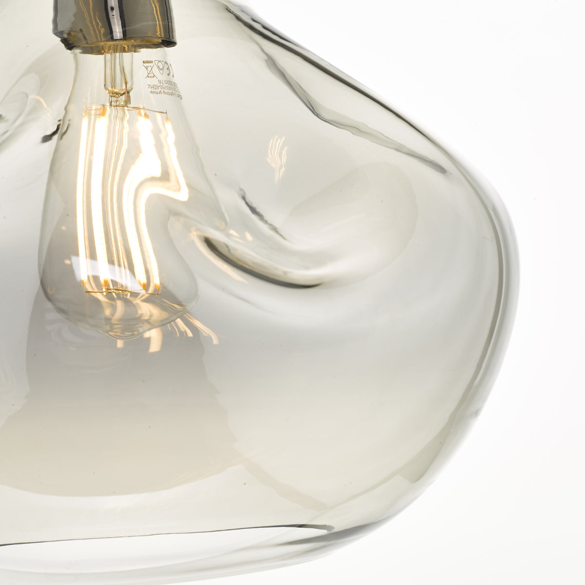 Close-up of a clear, irregularly shaped glass pendant light with a glowing filament bulb inside.