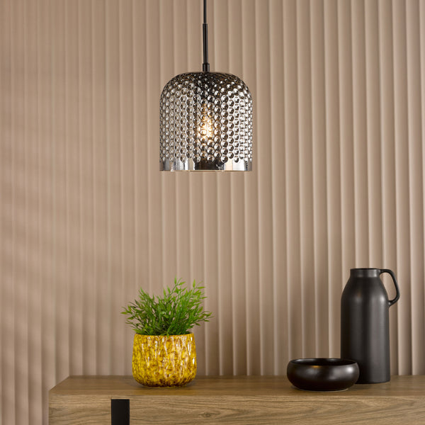 Silver dimpled pendant light with a plant in a yellow pot and black vase on a wooden surface
