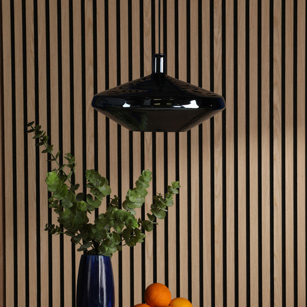 Black pendant light hanging above a blue vase with greenery and oranges on a wooden slatted wall.