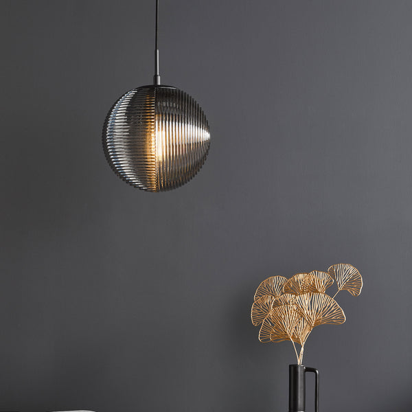 A modern ribbed glass pendant light hangs above a black vase with gold decorative leaves.