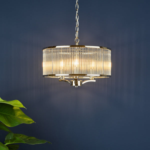 Round chandelier with clear fluted glass shade and gold metal frame, hanging against a dark blue wall