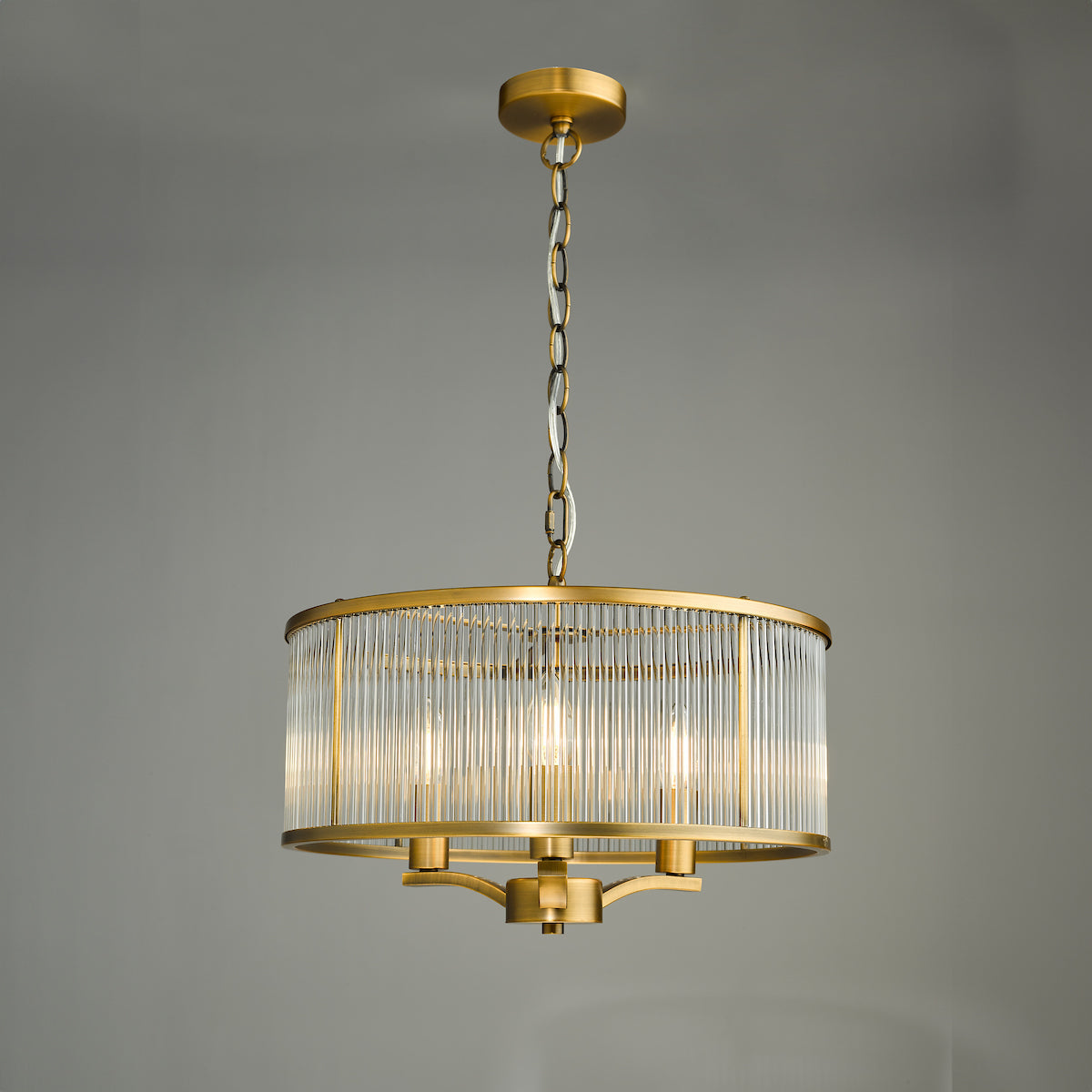 A gold chandelier with a cylindrical glass shade and three exposed bulbs.
