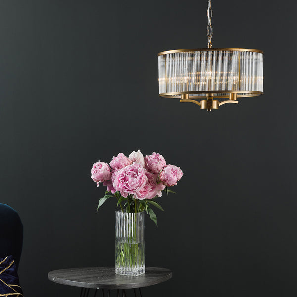 Pink peonies in a clear vase on a round table with a gold and glass chandelier above.