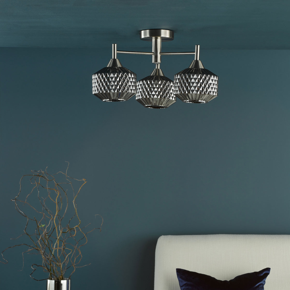 Three light ceiling fixture with textured glass shades, above a white headboard and a vase with branches