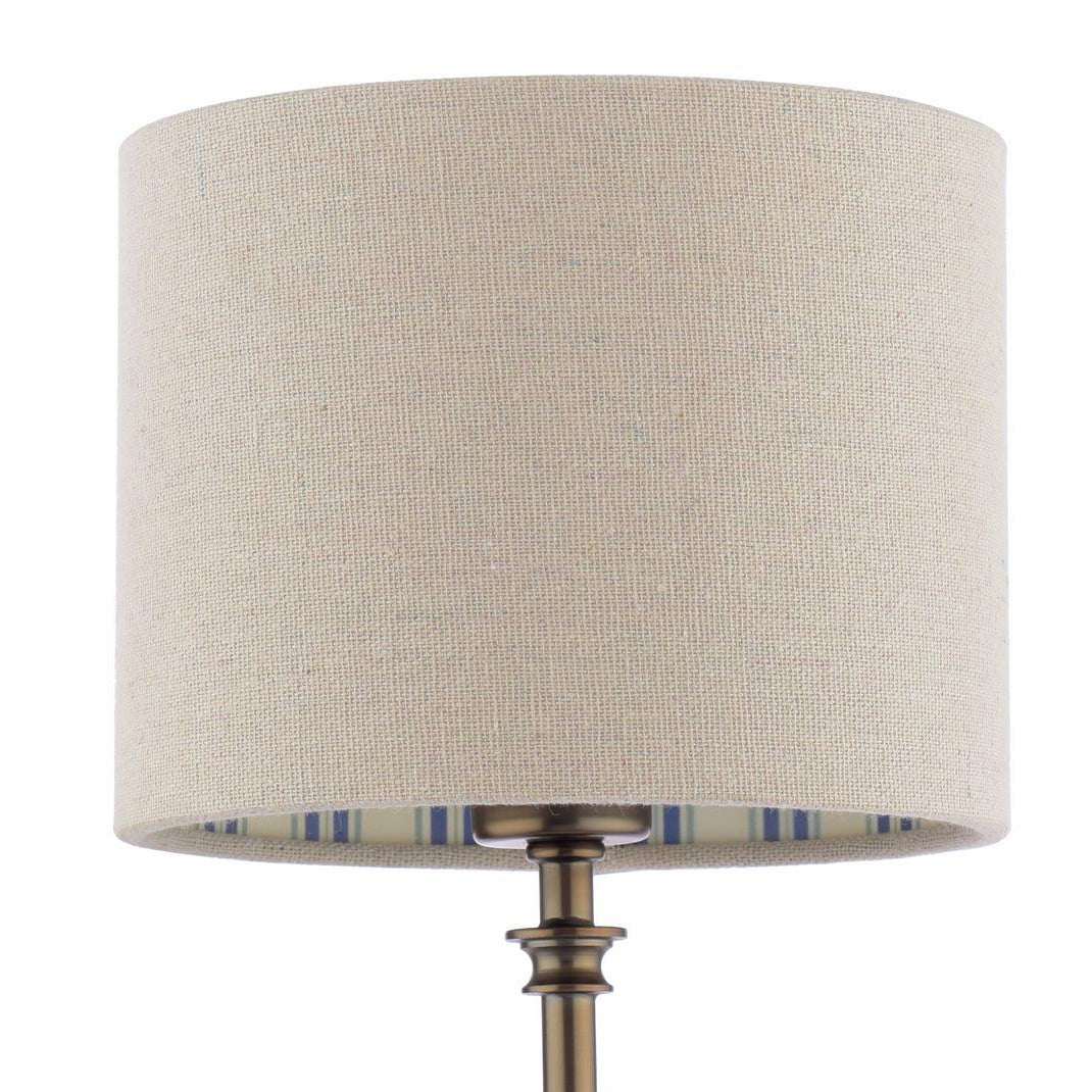 Beige linen drum lampshade with blue striped interior lining on a bronze lamp base