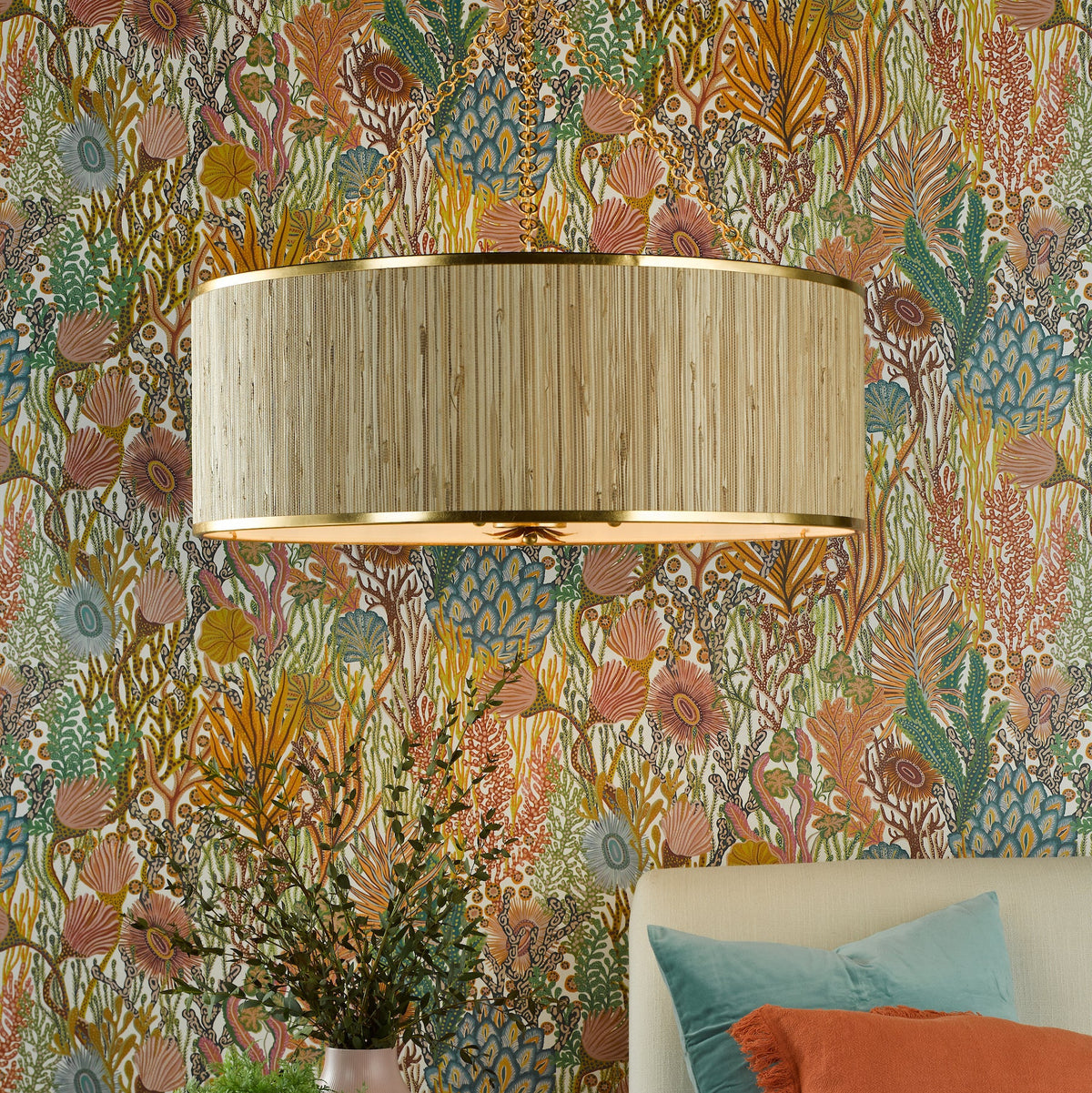 A beige drum shade light fixture with gold trim on a wall with colorful coral reef wallpaper