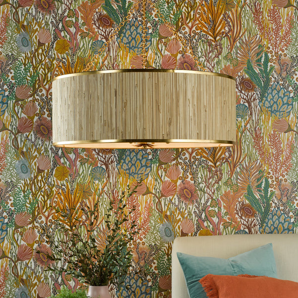 A beige drum shade light fixture with gold trim on a wall with colorful coral reef wallpaper