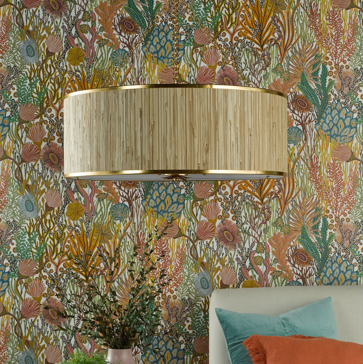 A close-up of a wall sconce with a woven shade and gold trim, against a colorful botanical wallpaper