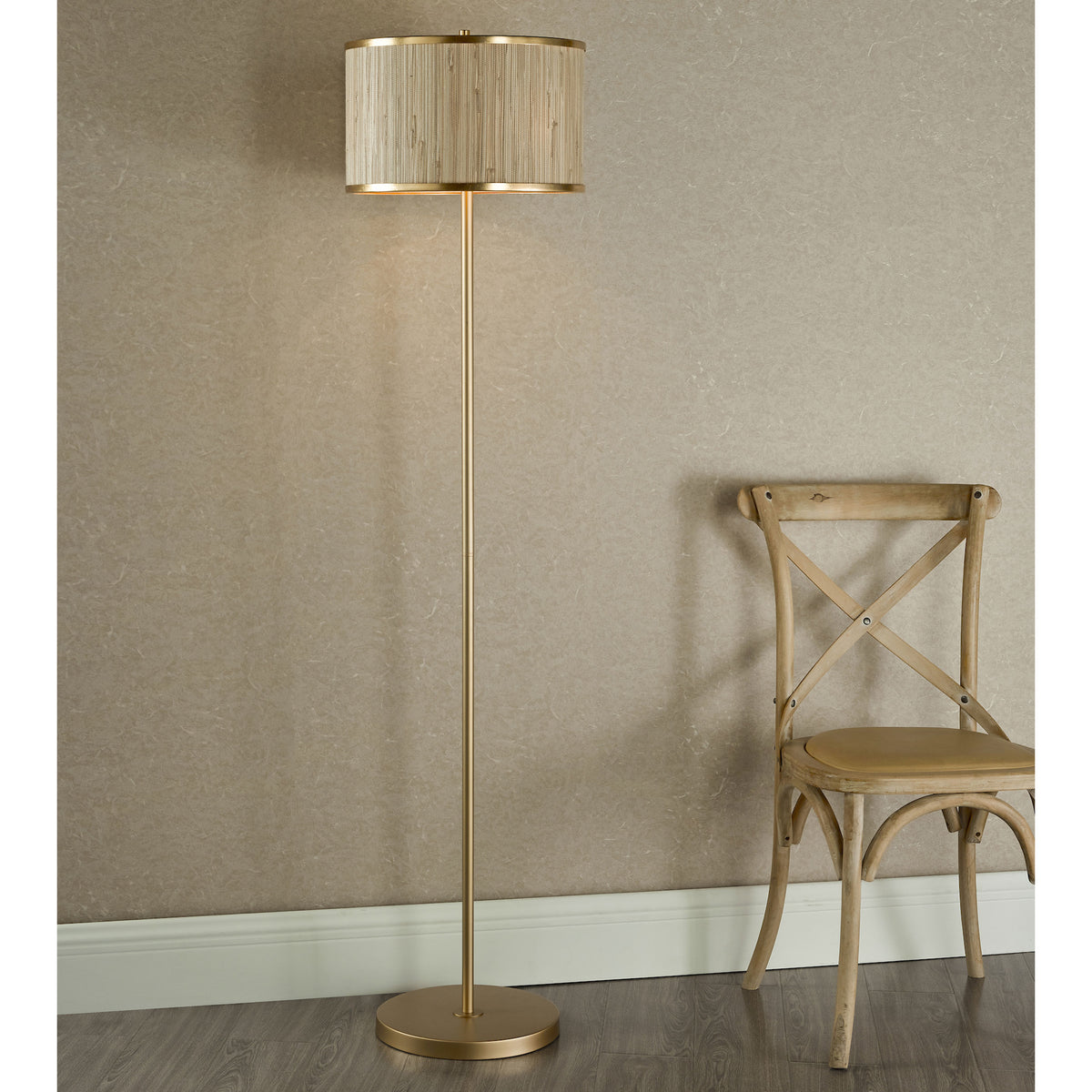 Tall gold floor lamp with a textured cylindrical shade next to a light wood chair with a cross back.
