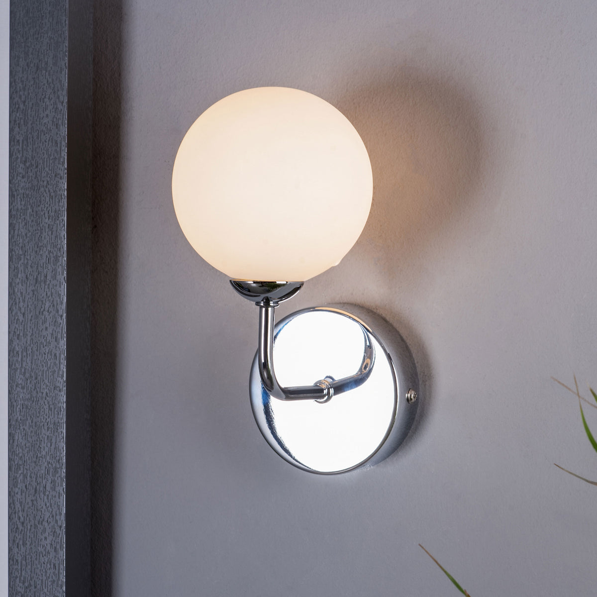 A modern wall sconce with a glowing spherical white glass shade and a polished chrome base.