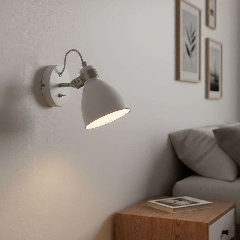 White wall light with a curved arm and a bell-shaped shade, illuminating a wall above a wooden bedside table