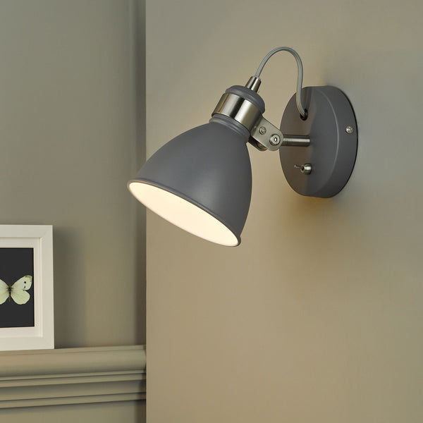 Grey wall light with a brushed steel arm and a toggle switch, illuminating a wall and a framed butterfly print