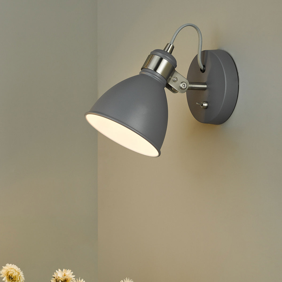 Grey metal wall light with a cone-shaped shade and a toggle switch, mounted on a light grey wall