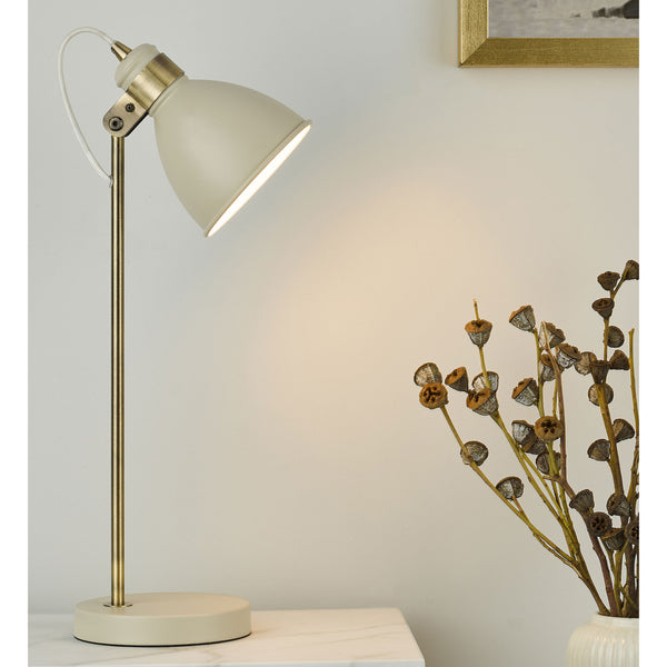 Cream desk lamp with brass accents and a white braided cord, next to a vase of dried seed pods