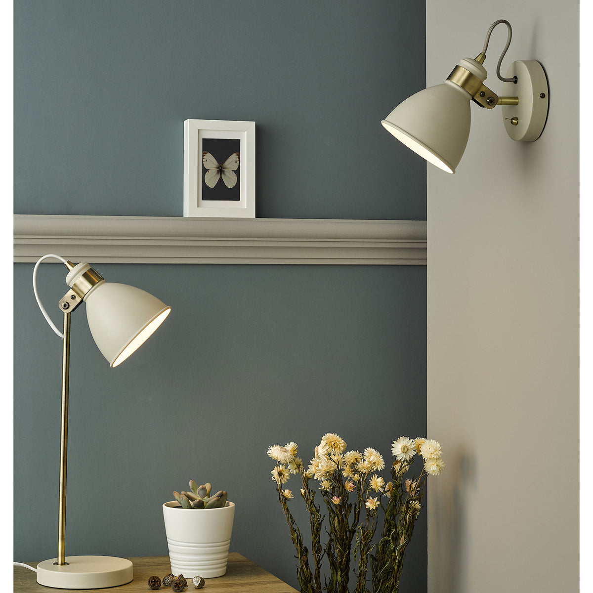 Cream and brass wall light and matching table lamp on a wooden surface with a plant and dried flowers