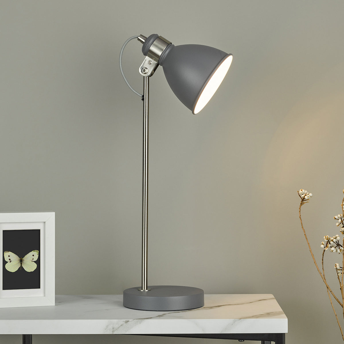 Grey desk lamp with a silver stand and base, on a white marble table