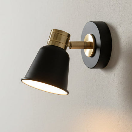 Black and brass wall light with a conical shade, mounted on a white wall