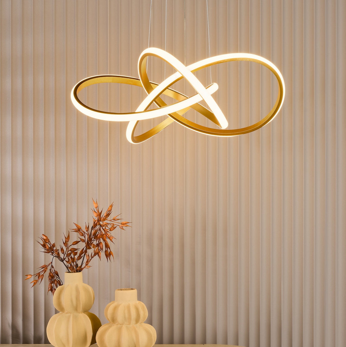 Gold chandelier with intertwined rings, illuminated with LED lights, hanging above two decorative vases