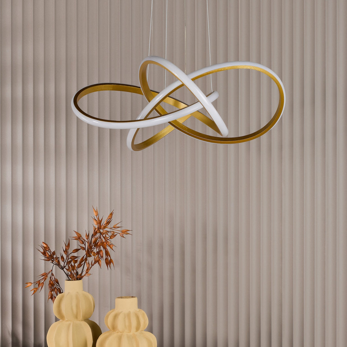 Modern chandelier with intertwined white and gold rings, hanging above two decorative yellow vases with dried foliage