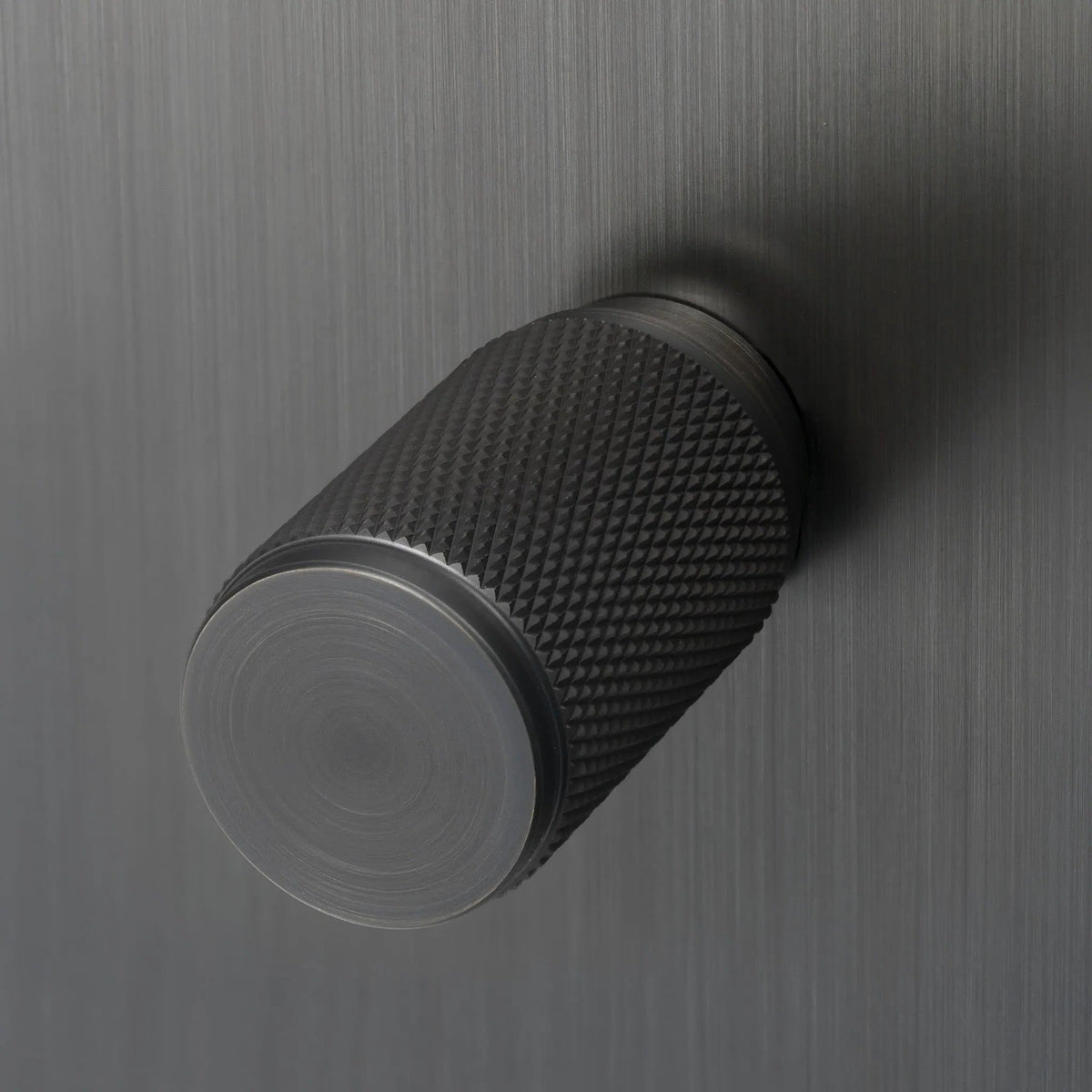 Knurled metal knob in a dark finish on a brushed metal surface