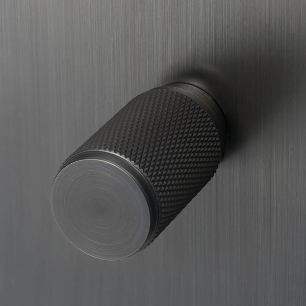 Knurled metal knob in a dark finish on a brushed metal surface