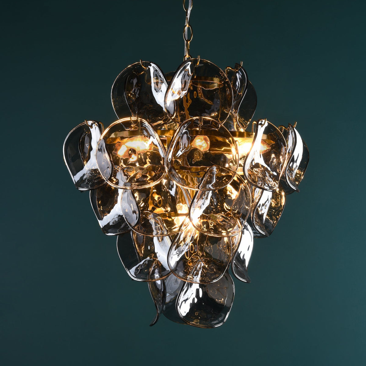 Chandelier with multiple clear glass petals and warm glowing bulbs against a dark teal background