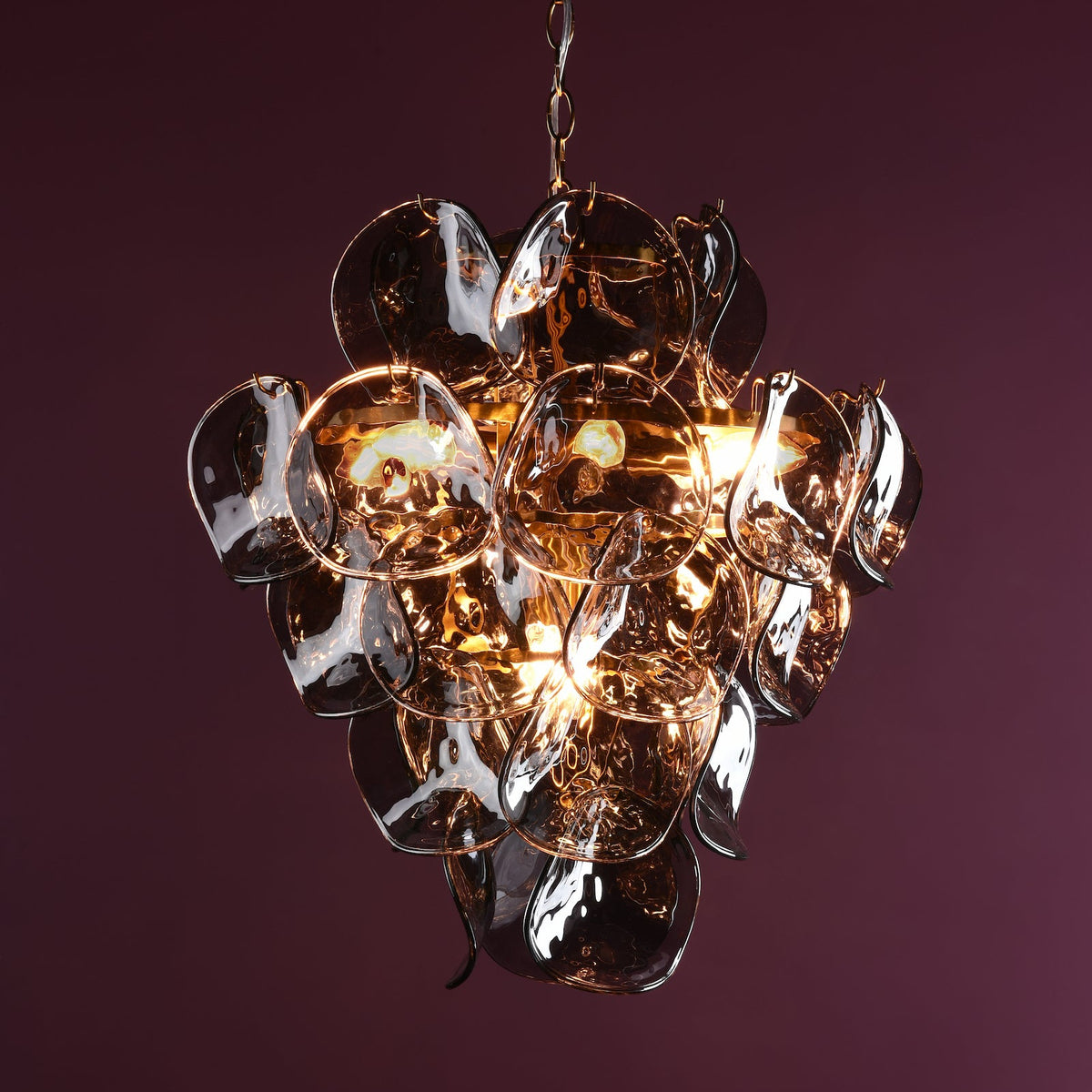 Chandelier with multiple glass petals in a dark amber color, illuminated from within, against a deep purple background