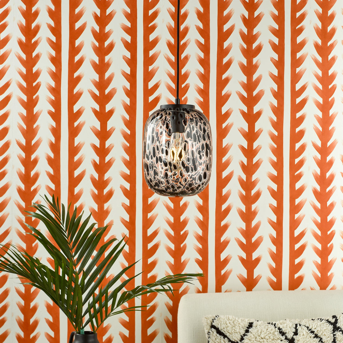 Orange and white patterned wallpaper with a hanging light fixture, plant, and sofa