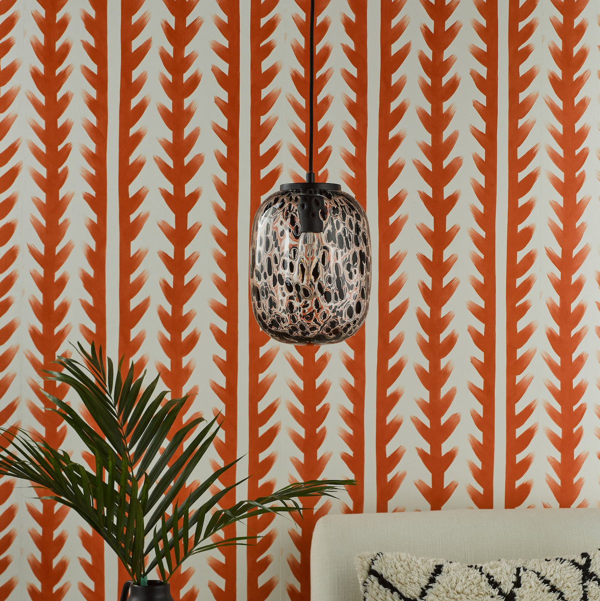 Orange and white patterned wallpaper with a black and orange speckled pendant light, a plant, and a sofa