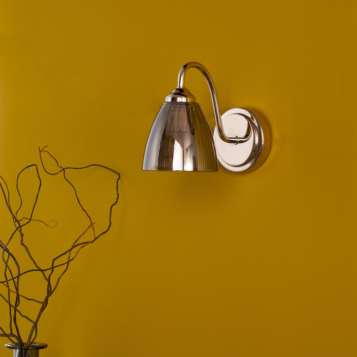 Polished nickel wall light with a fluted glass shade on a mustard yellow wall