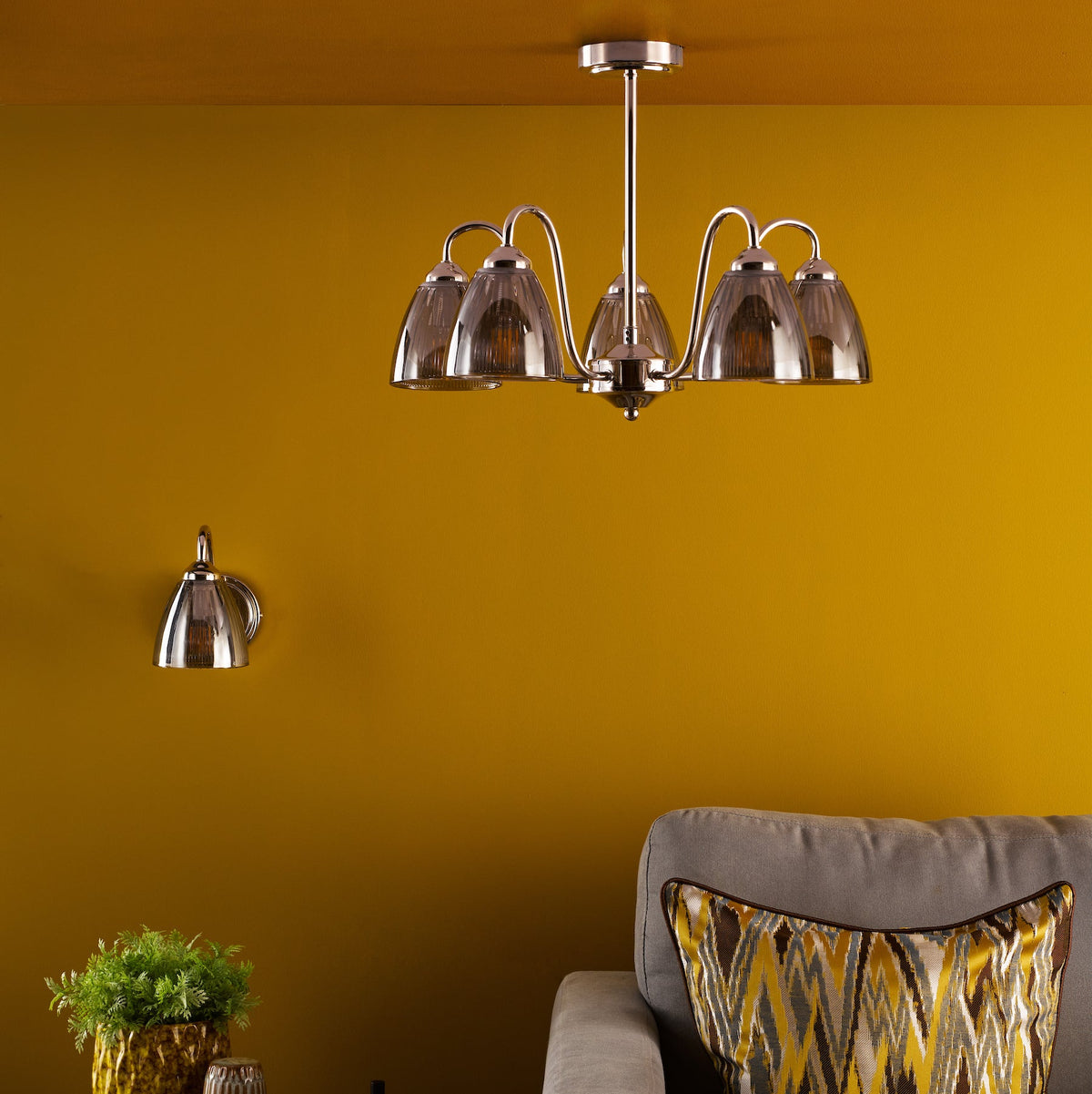 Polished chrome chandelier with five smoked glass shades and a matching wall light on a yellow wall