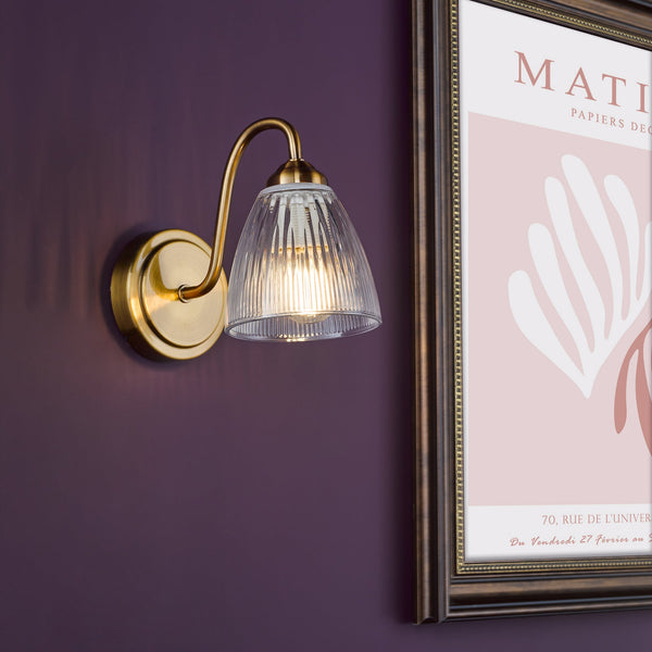 Brass wall light with a ribbed glass shade and a framed art print on a purple wall