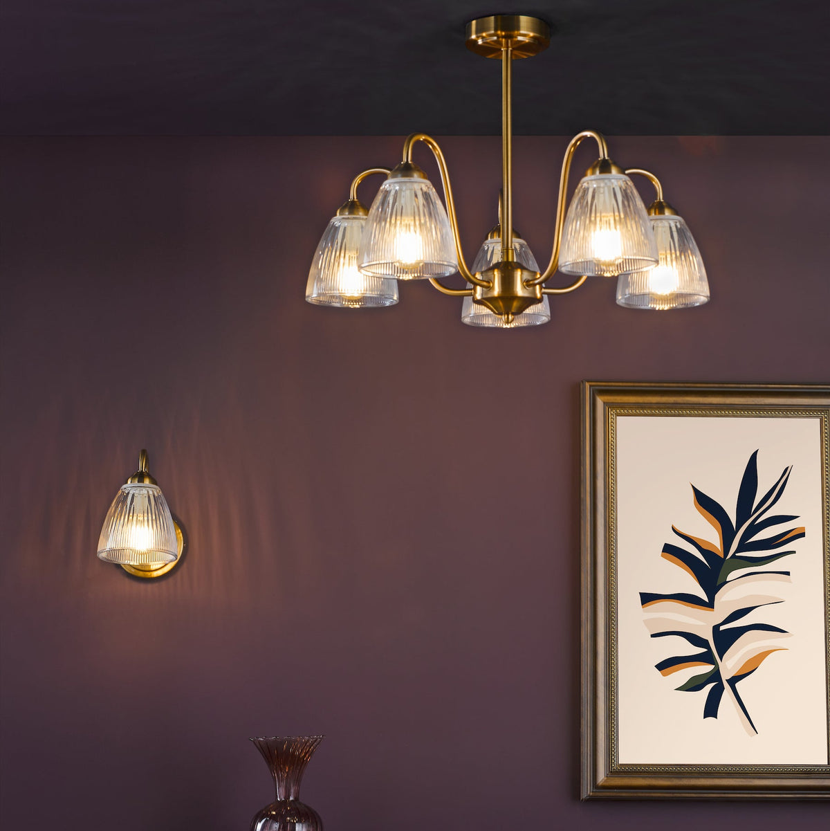 Brass chandelier with five ribbed glass shades and a matching wall sconce on a dark purple wall