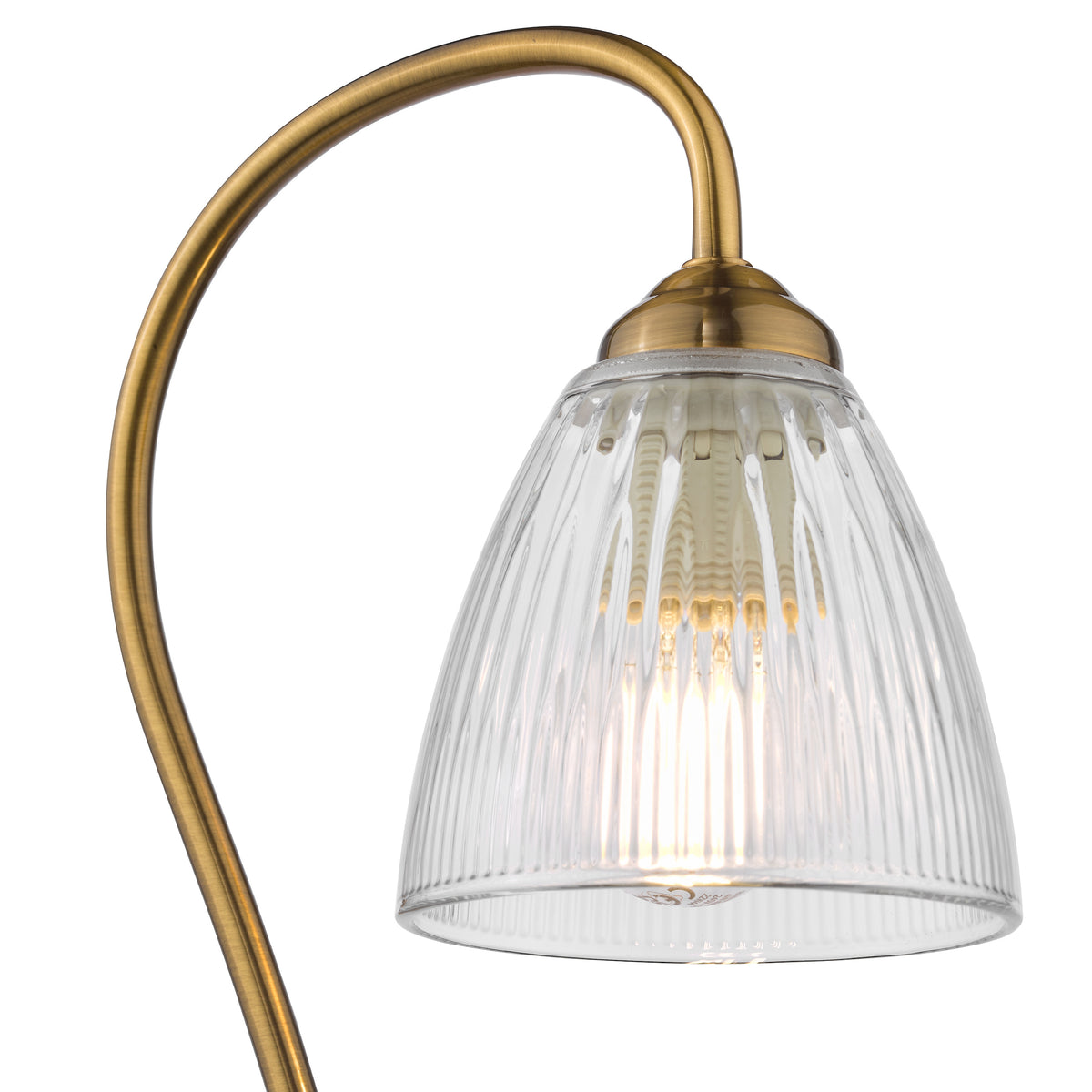 Close up of a brass lamp with a clear, ribbed glass shade and an illuminated bulb