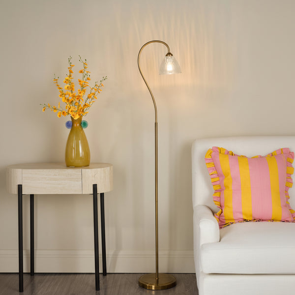Curved brass floor lamp with a fluted glass shade next to a white armchair and a side table