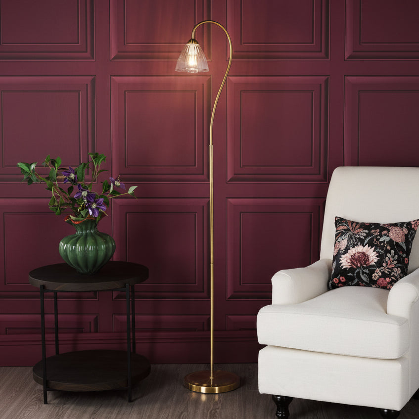 Brass floor lamp with a fluted glass shade next to a white armchair and a green vase with flowers