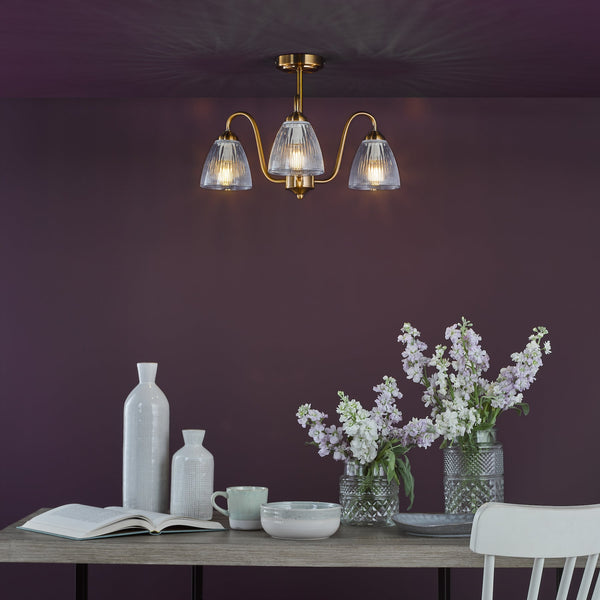Brass chandelier with three fluted glass shades illuminating a dining table with flowers and ceramics