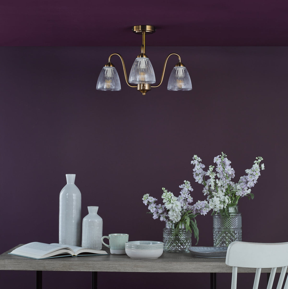 Brass chandelier with three fluted glass shades above a dining table with flowers and decor
