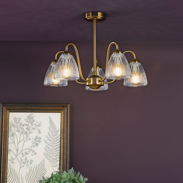 Brass chandelier with five ribbed glass shades, illuminating a dark purple room with a framed botanical print